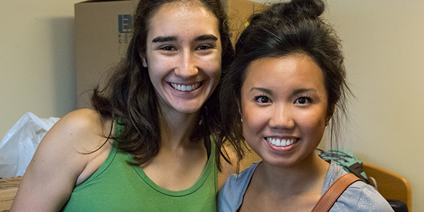 Two female students smiling with moving boxes in background
