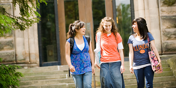 Three female students walking in front of building entrance on campus